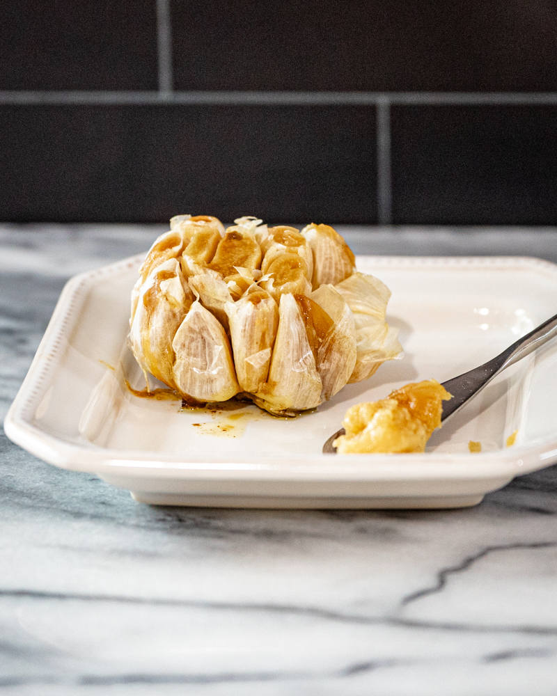 Roasted garlic, a whole head, on a plate with a little spreader.