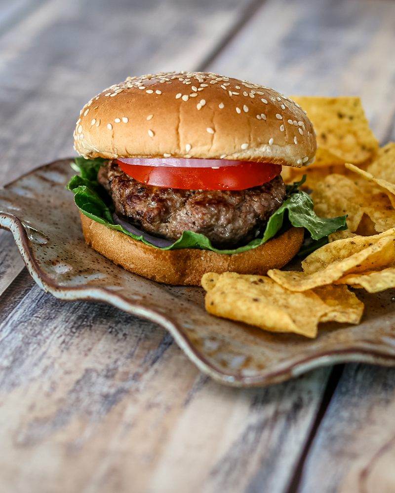 bacon and cheese stuffed burgers on a plate with chips on the side