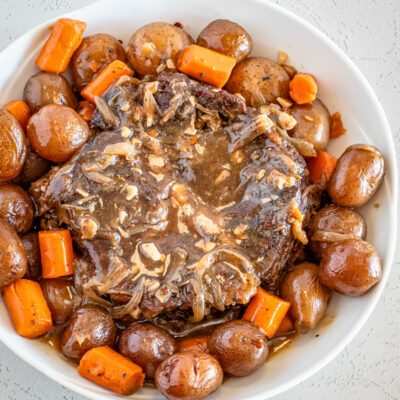 A slow cooker pot roast surrounded by potatoes and carrots.