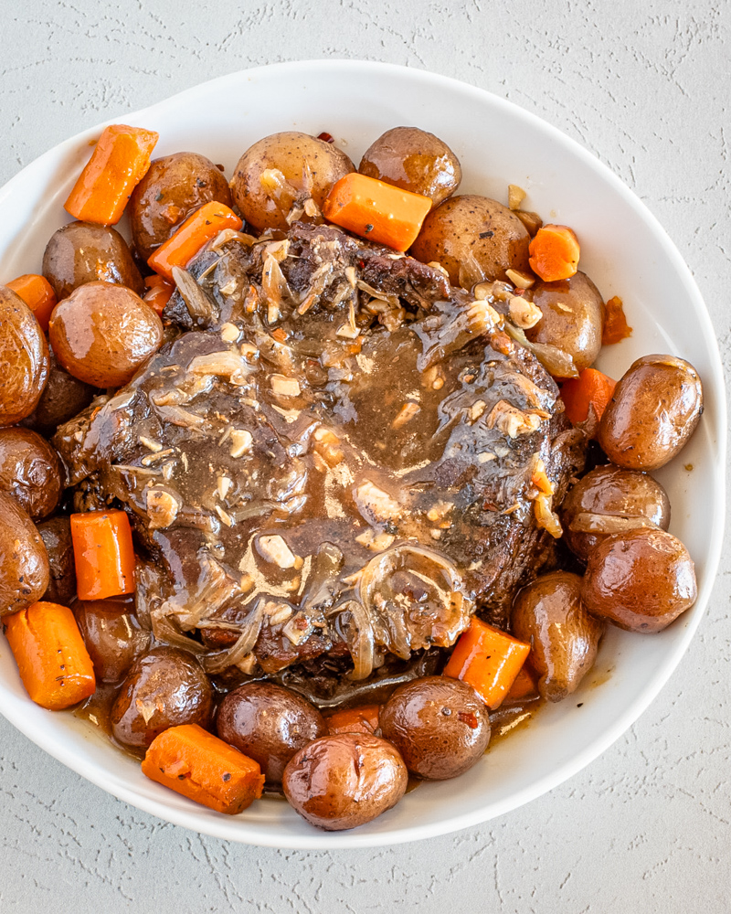 A slow cooker pot roast surrounded by potatoes and carrots.