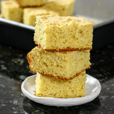 Sour cream cornbread squares stacked with the pan in the background
