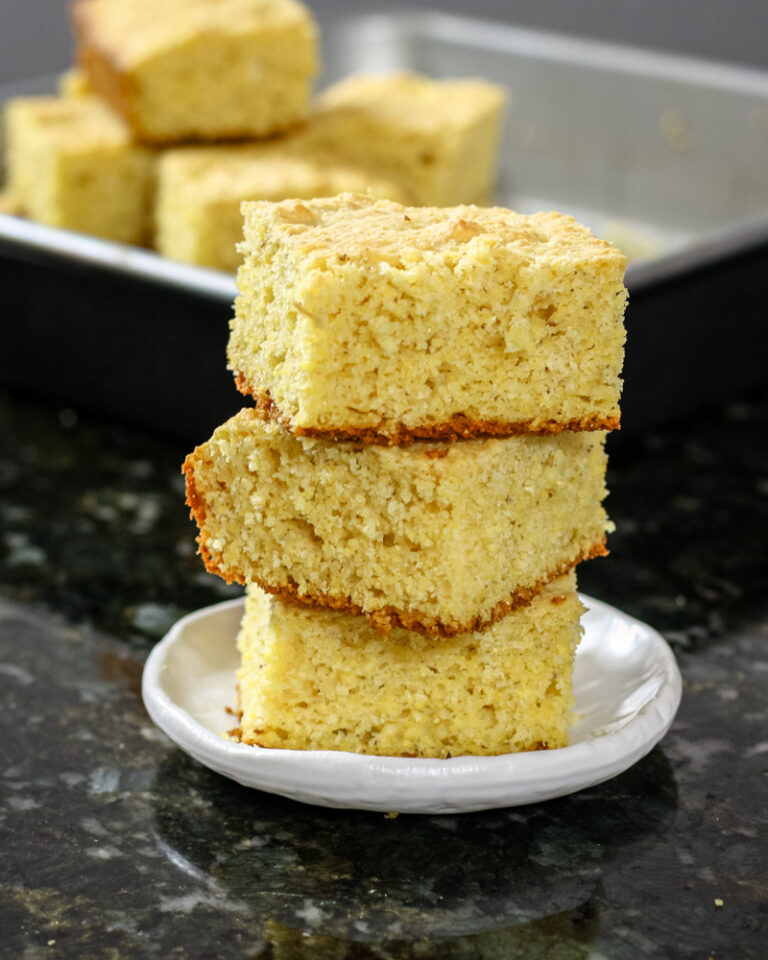 Sour cream cornbread squares stacked with the pan in the background