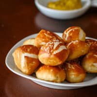 A plate of soft pretzel bites with some mustard in the background.