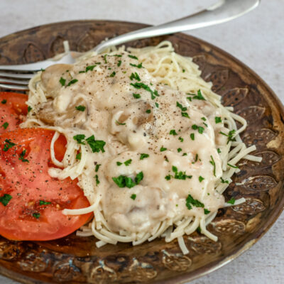 slow cooker chicken parisienne over pasta with sliced tomatoes on the side