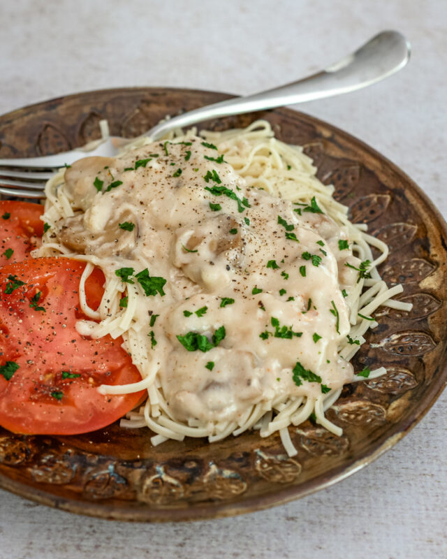 slow cooker chicken parisienne over pasta with sliced tomatoes on the side