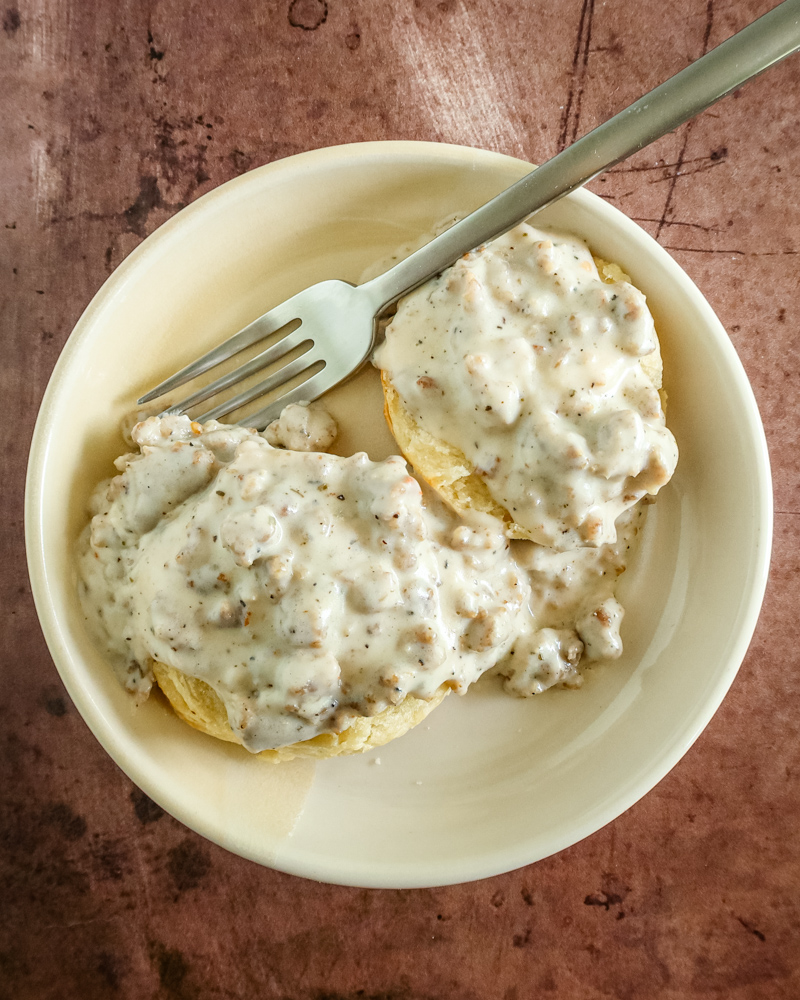 Biscuits and sausage gravy in a small bowl with fork.