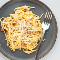Spaghetti carbonara on a plate with fork and parmesan cheese topping