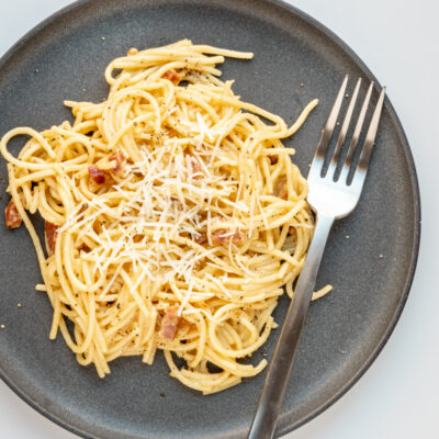 Spaghetti carbonara on a plate with fork and parmesan cheese topping