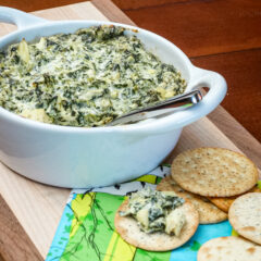 spinach artichoke dip in a baking dish with crackers on the side