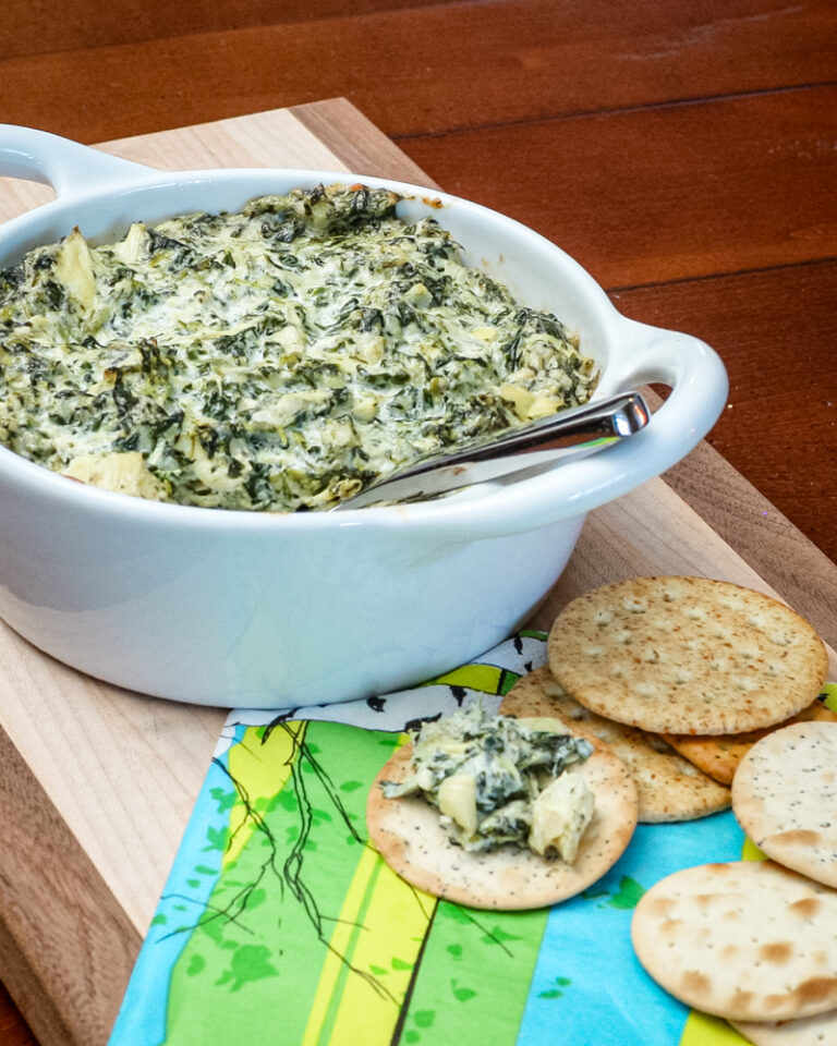 spinach artichoke dip in a baking dish with crackers on the side