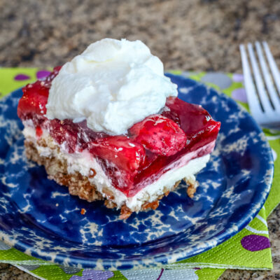 A strawberry dessert with a cream cheese layer and pretzel base, on a plate and topped with whipped topping.