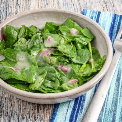 A serving of wilted spinach salad in a bowl