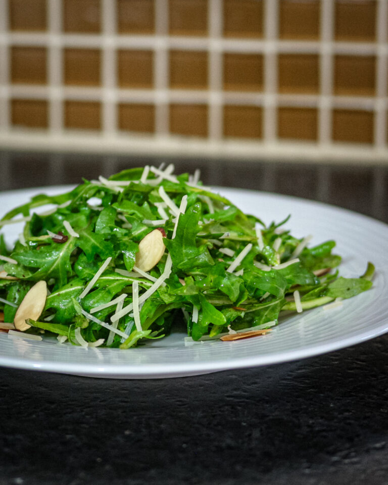 A simple arugula salad with sliced almonds on a plate