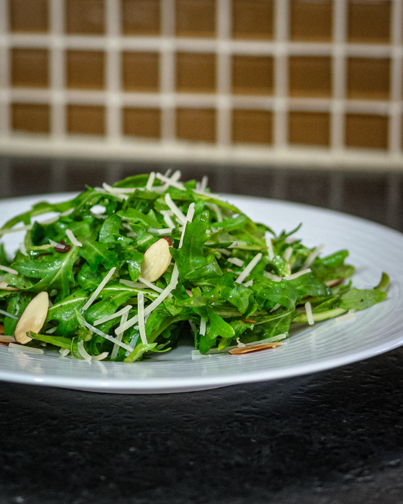A simple arugula salad with sliced almonds on a plate