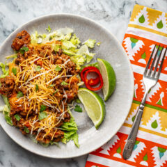Beef and bean taco casserole shown in a pan with cheese topping and lime wedges.