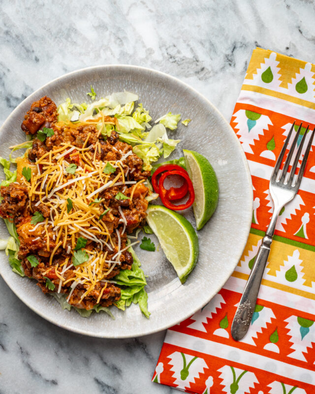 Beef and bean taco casserole shown in a pan with cheese topping and lime wedges.