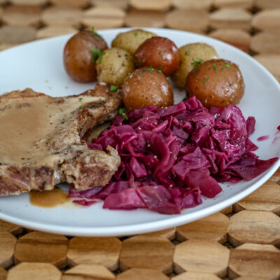 Braised red cabbage is shown with a pork chop and baby potatoes on a plate