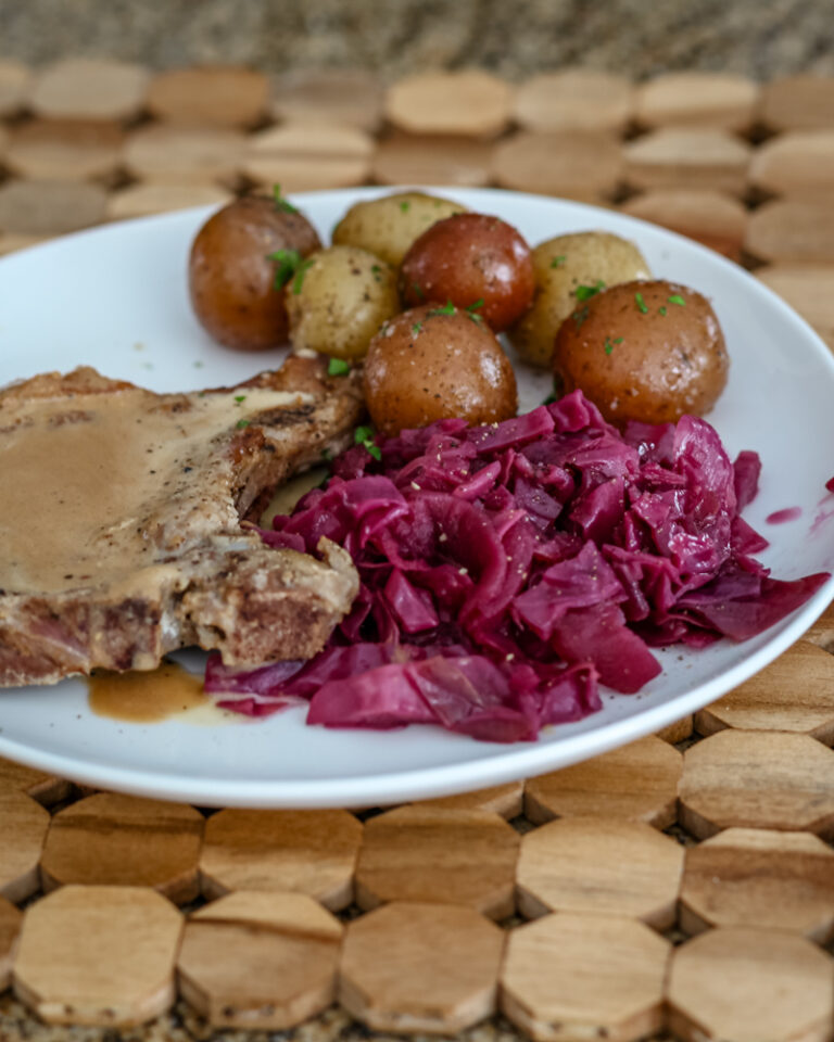 Braised red cabbage is shown with a pork chop and baby potatoes on a plate
