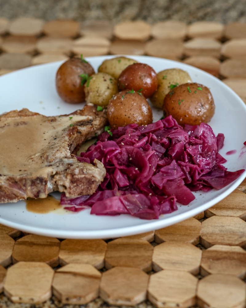 Braised red cabbage is shown with a pork chop and baby potatoes on a plate