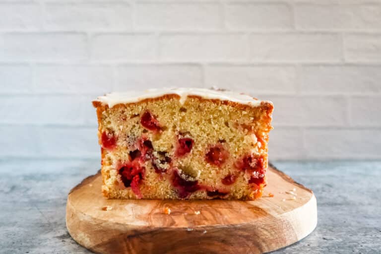 A loaf of iced cranberry orange bread, sliced, on a cutting board.