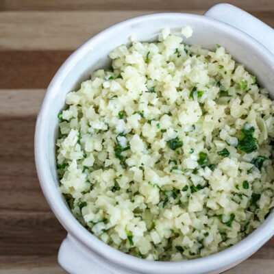 A bowl of cauliflower rice with garlic, parmesan cheese, and parsley