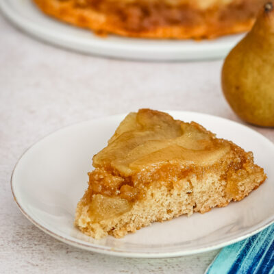 Baked pear upside-down cake slice on white plate.