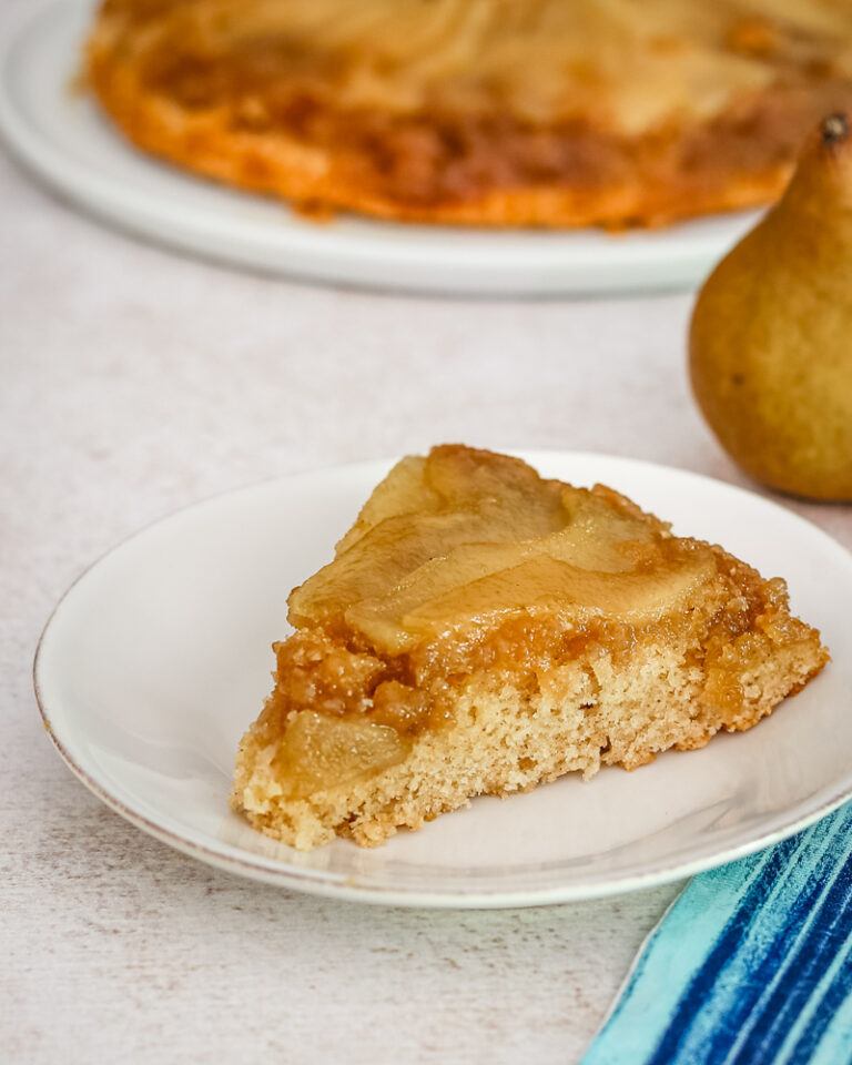 Baked pear upside-down cake slice on white plate.