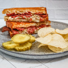 Reuben sandwich on a plate with chips and pickles