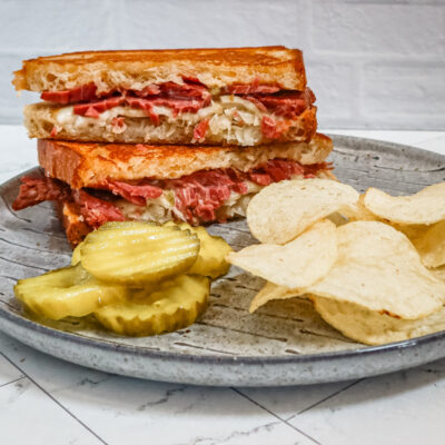 Reuben sandwich on a plate with chips and pickles
