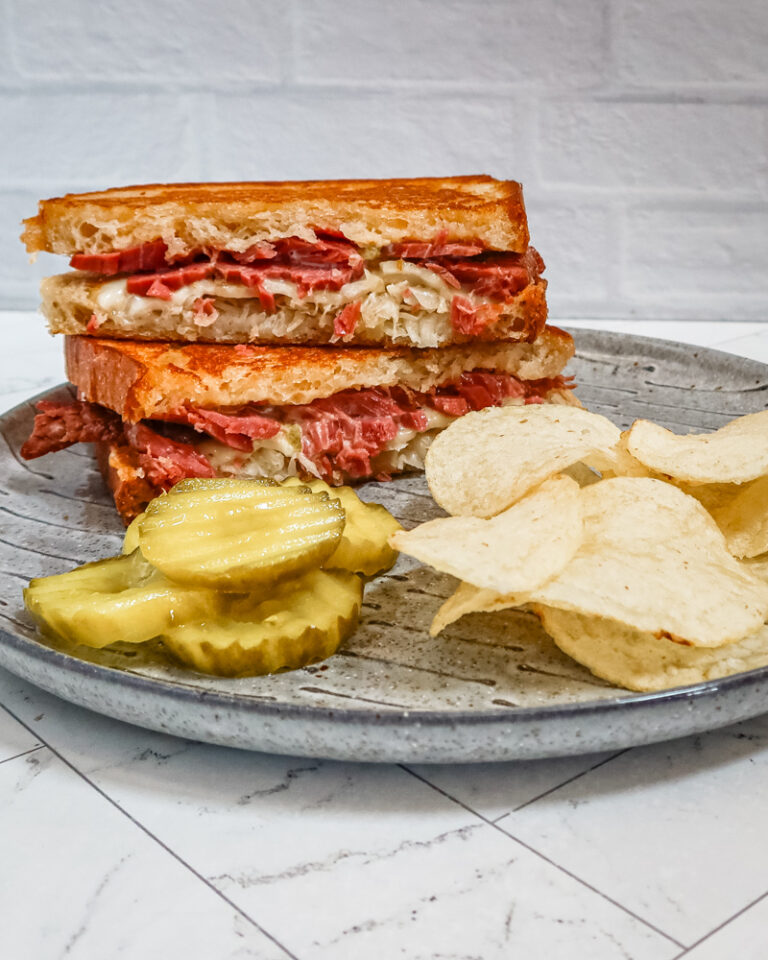 Reuben sandwich on a plate with chips and pickles