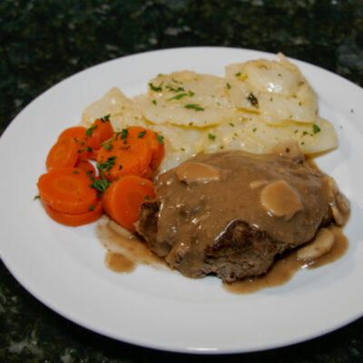 Salisbury steaks on a plate with scalloped potatoes and carrots