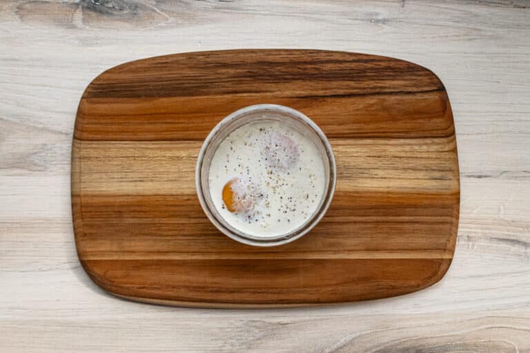 Shirred eggs prep in a glass ramekin.