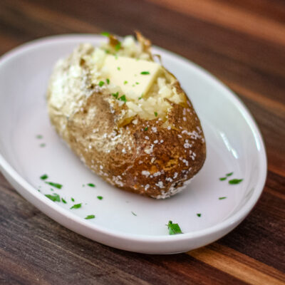 A baked potato on a plate with butter and parsley