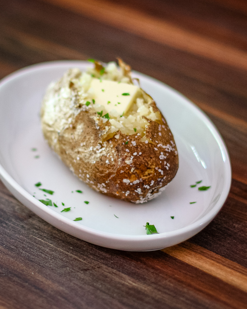 A baked potato on a plate with butter and parsley
