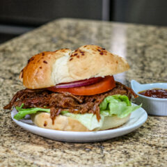 barbecue beef sandwich on a small plate with barbecue sauce on the side.