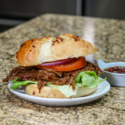 barbecue beef sandwich on a small plate with barbecue sauce on the side.
