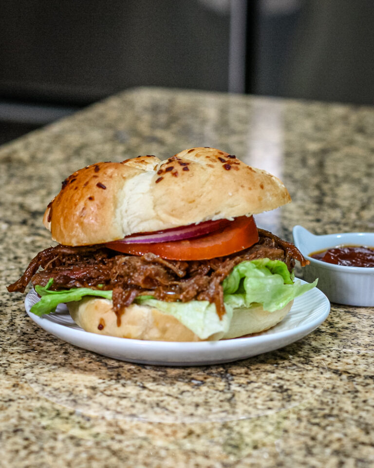 barbecue beef sandwich on a small plate with barbecue sauce on the side.