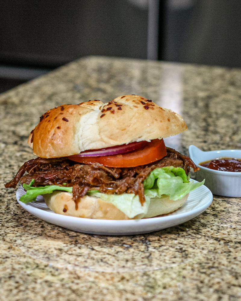 barbecue beef sandwich on a small plate with barbecue sauce on the side.