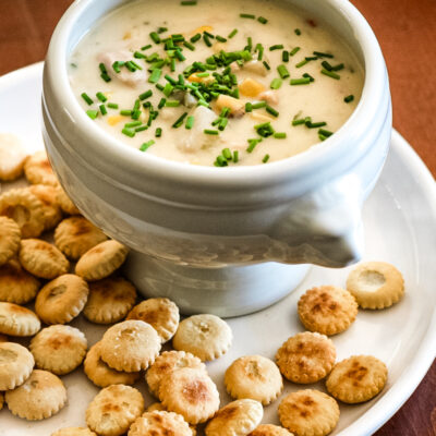A bowl of tuna and corn chowder with oyster crackers on the plate.