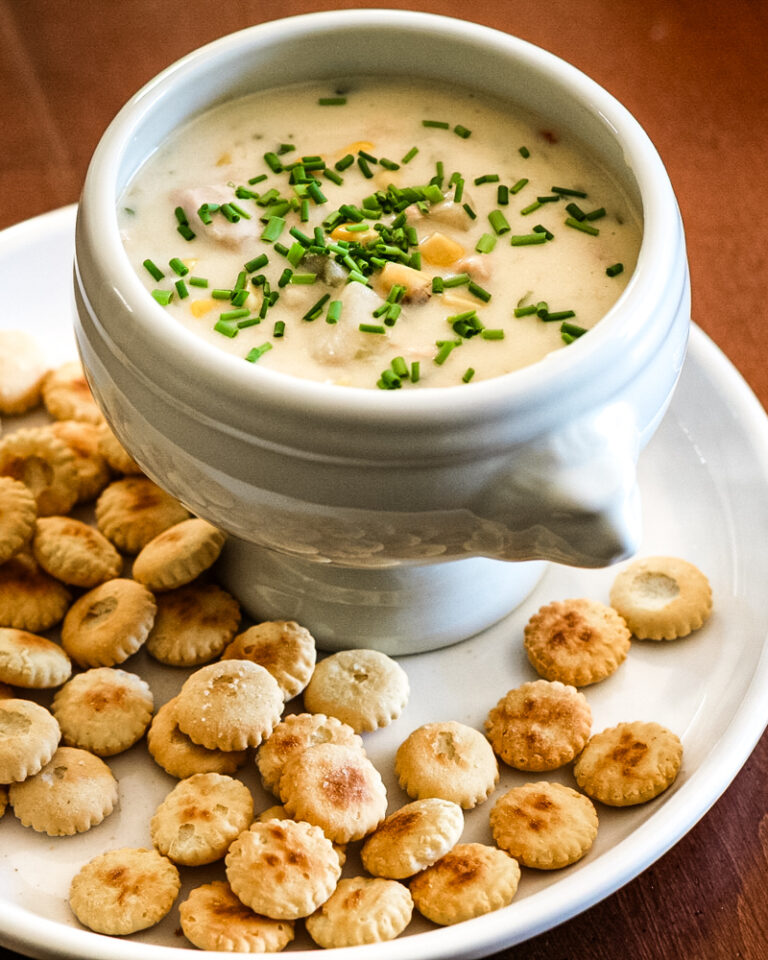 A bowl of tuna and corn chowder with oyster crackers on the plate.