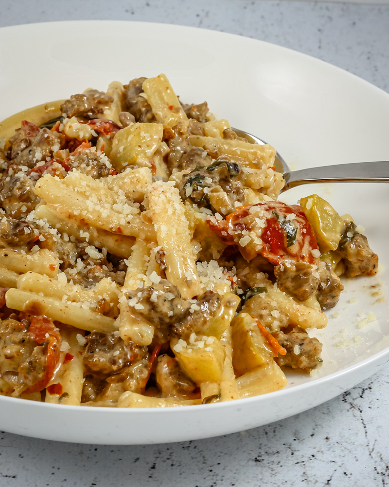 Tuscan pasta in a bowl with italian sausage, sun dried tomatoes, and zucchini