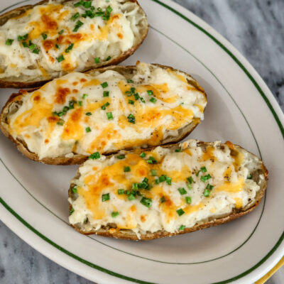A platter with twice baked potatoes with cheese and chives for topping.