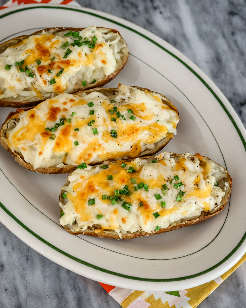 A platter with twice baked potatoes with cheese and chives for topping.