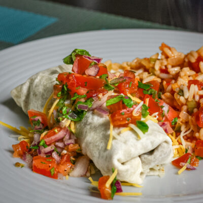 Beef and bean burritos on a plate with Mexican rice and salsa.