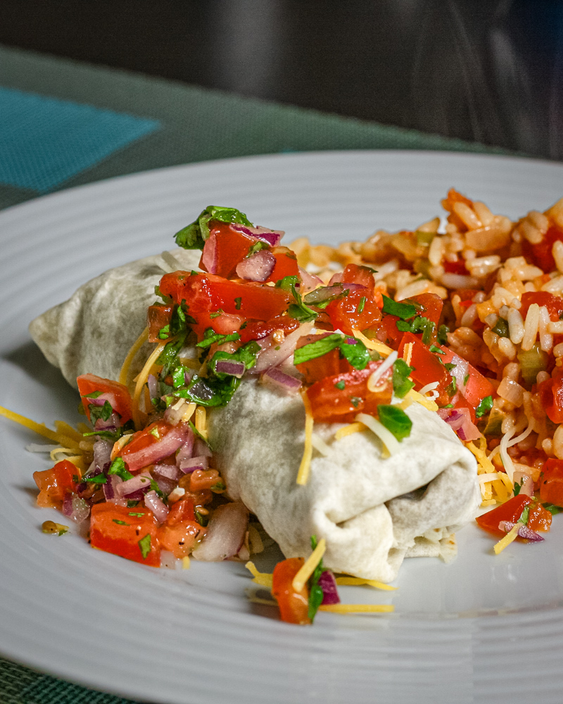 Beef and bean burritos on a plate with Mexican rice and salsa.