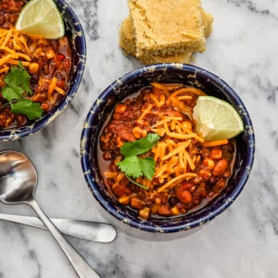 Beef and bean chili in bowls with garnishes and cornbread.