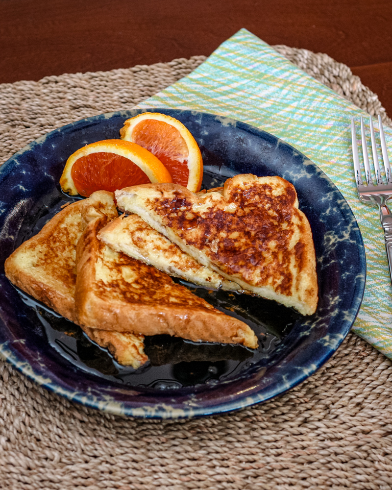 Sliced French toast on a plate with orange wedges on the side.