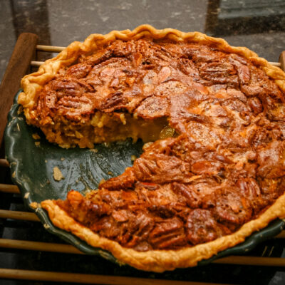 A pecan pie on a wooden rack with a sliced taken out.