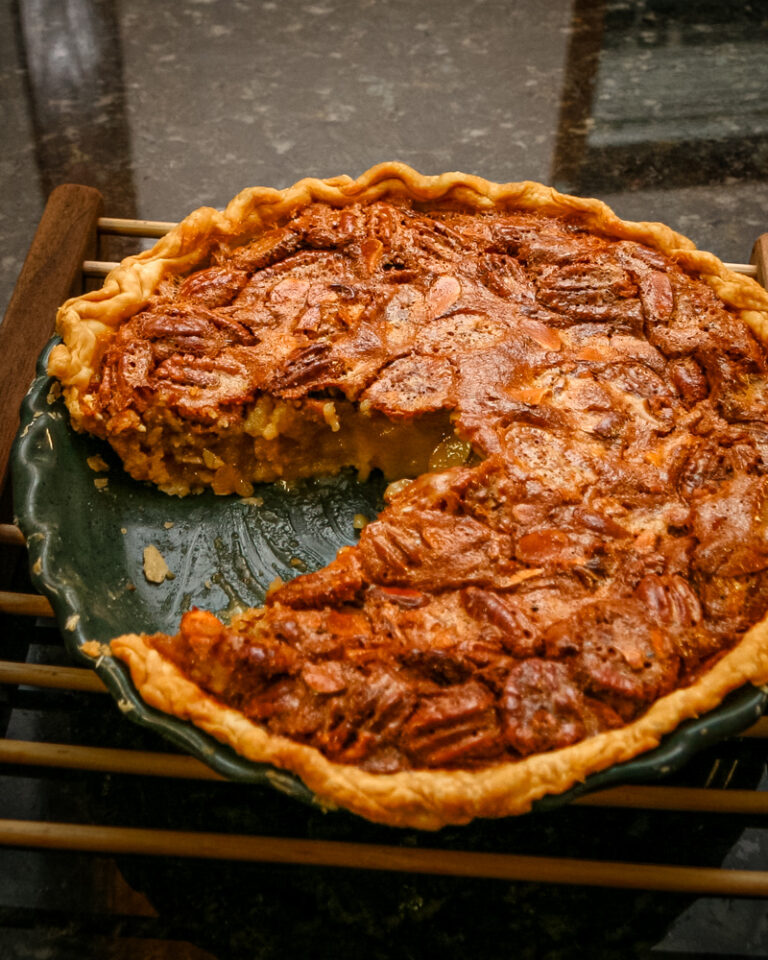 A pecan pie on a wooden rack with a sliced taken out.