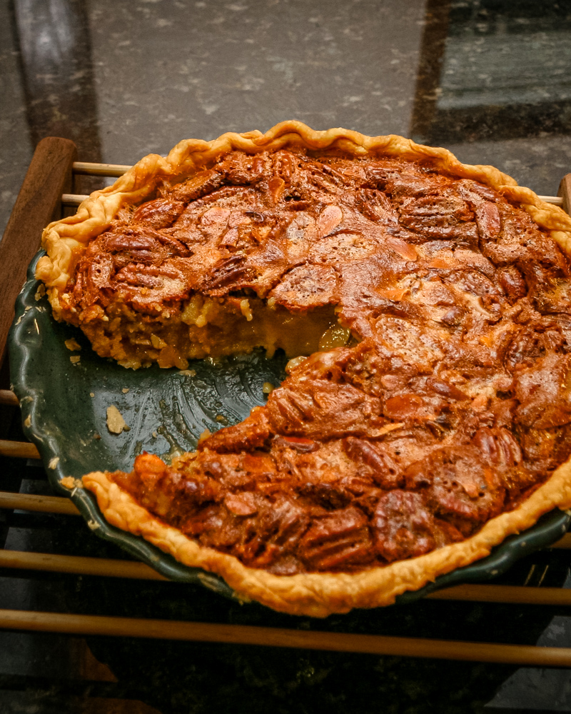 A pecan pie on a wooden rack with a sliced taken out.